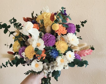 May include: A bouquet of dried flowers in shades of yellow, orange, purple, and white. The bouquet includes daisies, sunflowers, and other wildflowers.