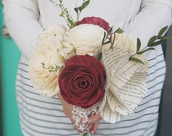 Puede incluir: Un ramo de flores de madera de sola blanca y burdeos con vegetación y una página de libro envuelta alrededor de los tallos. La página del libro tiene texto de la novela "Twilight" de Stephenie Meyer.