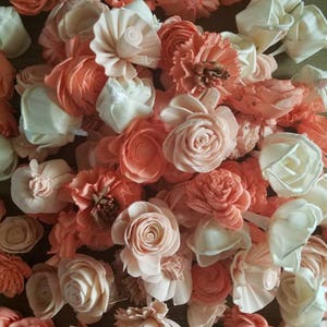 May include: A collection of peach and cream colored sola wood flowers. The flowers are arranged in a pile and are all different sizes and shapes.