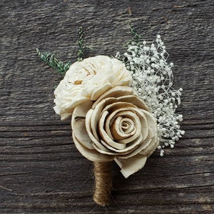 May include: A small bouquet of white sola wood flowers with a burlap stem. The flowers are arranged in a cluster with a single larger rose-shaped flower in the center.