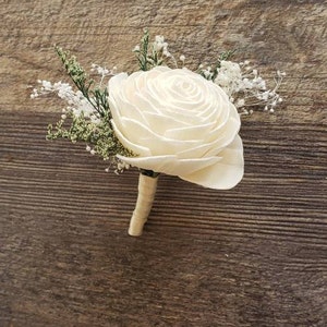 May include: A white sola wood flower boutonniere with small white and green sprigs.
