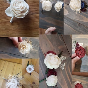 May include: A collection of nine white and red wooden flower boutonnieres with greenery and small white flowers. The boutonnieres are arranged on various wooden surfaces.
