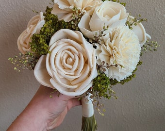 May include: A bouquet of white sola wood flowers with green foliage. The bouquet is tied with a white ribbon.