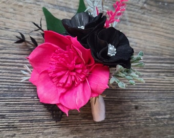 May include: A pink and black flower arrangement with a single pink flower and two black flowers with rhinestones. The flowers are arranged on a wooden surface.