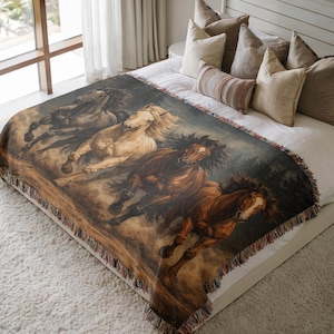 May include: A woven throw blanket featuring a painting of four horses running. The horses are in shades of black, tan, and brown, with flowing manes and tails. The blanket has a fringed edge and is displayed on a bed.