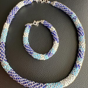 Peut inclure: Un ensemble collier et bracelet de perles. Le collier et le bracelet sont faits de petites perles rondes dans les tons de bleu, blanc et argent. Le collier est de style ras du cou et le bracelet est de taille standard. Les deux pièces ont un fermoir argenté.