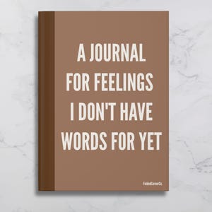 Peut inclure: Un journal marron avec le texte "A JOURNAL FOR FEELINGS I DON'T HAVE WORDS FOR YET" en blanc. Le journal a une tranche marron et le nom de la marque "FoldedCornerCo." est imprimé en bas à droite.