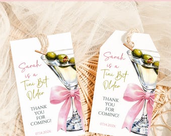 Può includere: Due etichette regalo bianche con illustrazioni di martini e fiocchi rosa. Le etichette recitano "Sarah is a Tini Bit Older" e "Thank You For Coming!" con una data. Le etichette hanno un cordino per appenderle.