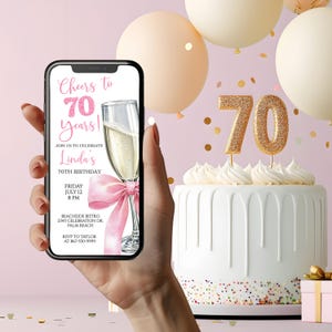 May include: A smartphone displays a birthday invitation with the text "Cheers to 70 years!" and a champagne glass with a pink bow. A white cake with gold glitter "70" candles and balloons are in the background.