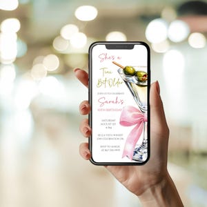 May include: A smartphone screen shows a digital invitation for a 50th birthday celebration. The design includes a martini glass with olives, a pink bow, and the text "She's a Tini Bit Older." The invitation provides event details and RSVP information.