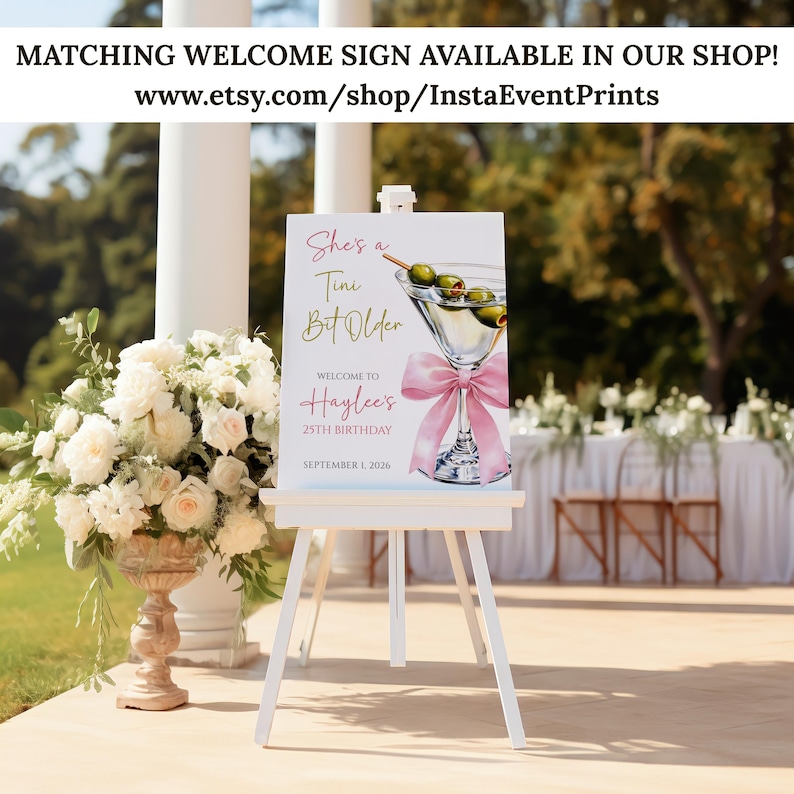 May include: A white easel displays a welcome sign with a martini glass illustration and the text "She's a Tini Bit Older" and "Welcome to Haylee's 25th Birthday September 1, 2026." The sign is decorated with a pink bow and olives. The background includes flowers and a table.