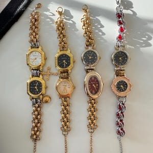 May include: A collection of vintage wristwatches with gold-toned and silver-toned metal bands. The watch faces are various shapes, including round, oval, and flower-shaped, with different colored dials. Some watches have decorative charms.
