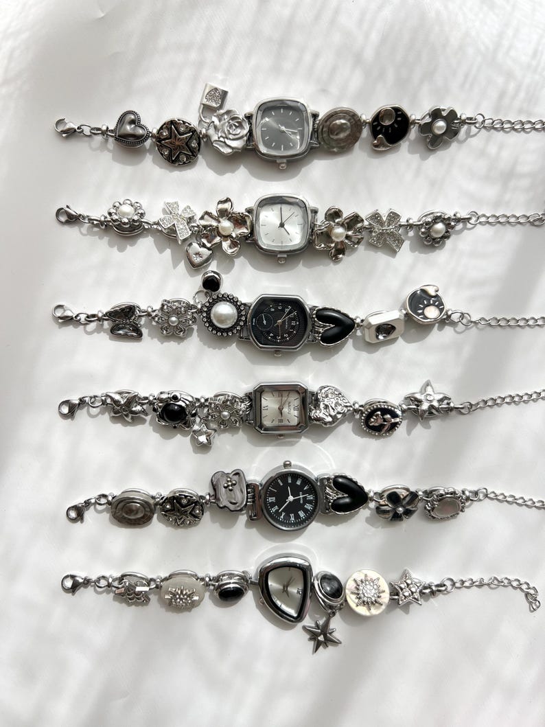 May include: Six silver bracelet watches with decorative charms such as hearts, stars, flowers, and geometric shapes. Each watch has a different face, with square and round dials. The bracelets are displayed on a white surface.