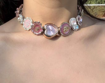 May include: A pink and gold charm necklace with a heart-shaped watch, flowers, and other decorative charms.
