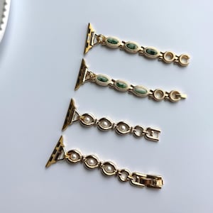 May include: Four gold-toned watch bands. Two bands feature green oval-shaped stones, while the other two have white pearl-like accents. Each band has a clasp and connector for attachment to a watch.