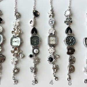 May include: Six silver charm bracelets, each with a different watch face and decorative charms. The bracelets feature square and round watch faces, and are adorned with charms such as stars, flowers, and hearts. They are displayed against a white background.