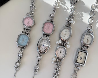 May include: Four silver-toned bracelet watches with various pastel-colored faces. Each watch has a different shape, including round, oval, and rectangular. The bracelets feature pearl and chain details, with a clasp closure.