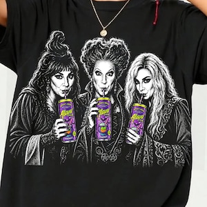 May include: A black t-shirt featuring a white graphic illustration of three women with elaborate hairstyles, each holding a purple Alani Nu energy drink can. The design is centred on the chest, showcasing detailed line work and shading.