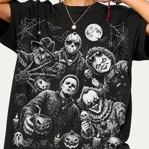 Può includere: Una t-shirt nera con una stampa grafica bianca di vari personaggi di film horror, tra cui una figura con maschera da hockey, un personaggio con artigli, una bambola e un clown, circondati da zucche, ragnatele, pipistrelli e una luna piena.