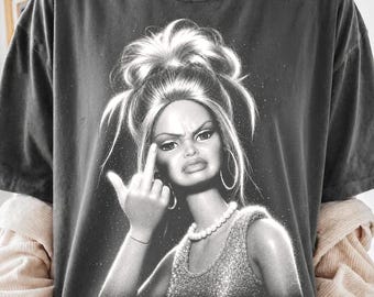 Może przedstawiać: Ciemnoszary t-shirt z krótkim rękawem z czarno-białym nadrukiem graficznym przedstawiającym lalkę z wysokim kokiem, noszącą perłowy naszyjnik i bezrękawnik, wykonującą gest środkowego palca z wyzywającym wyrazem twarzy.