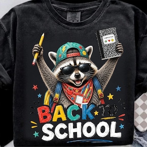 Puede incluir: Una camiseta negra de manga larga con el gráfico de un mapache que lleva una gorra de béisbol turquesa, gafas de sol y un pañuelo rojo. El mapache sostiene un lápiz amarillo y un cuaderno. El texto dice BACK TO SCHOOL en letras de colores.