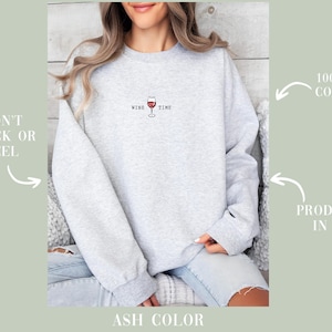 May include: Light gray sweatshirt with the words "WINE TIME" and a wine glass graphic. The sweatshirt is made of 100% US cotton and is produced in the USA. The text "WON'T CRACK OR PEEL" is also visible.