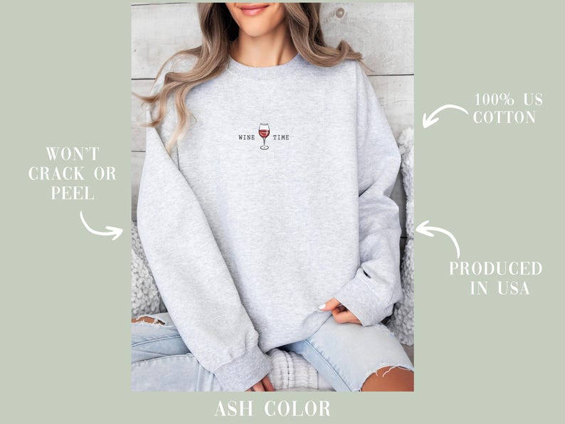 May include: Light gray sweatshirt with the words "WINE TIME" and a wine glass graphic. The sweatshirt is made of 100% US cotton and is produced in the USA. The text "WON'T CRACK OR PEEL" is also visible.