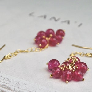 May include: A pair of gold earrings with a cluster of pink gemstone beads dangling from a chain.