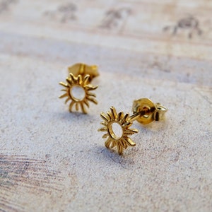 May include: A pair of gold sun stud earrings. The earrings are small and delicate, with a simple sun design.