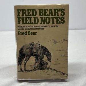 May include: A hardcover book titled "FRED BEAR'S FIELD NOTES" with a tan cover. The cover features a drawing of a horse carrying gear, a person, and a landscape. The text reads "A lifetime of outdoor lore and memories by one of the foremost bowhunters in the world."