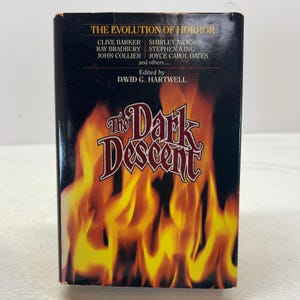 May include: A hardcover book titled The Dark Descent, edited by David G. Hartwell. The black cover features a prominent graphic of bright yellow and orange flames at the bottom and lists authors including Clive Barker and Stephen King in white text.