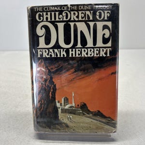 May include: A hardcover book titled "Children of Dune" by Frank Herbert. The cover features a desert landscape with a large rock formation and a city. The title is in large, stylized white letters against a black background.