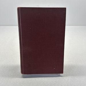 May include: A maroon-colored book with a textured cover. The book is standing upright, showcasing its rectangular shape and the subtle grain of the material. The spine is visible, indicating the binding.