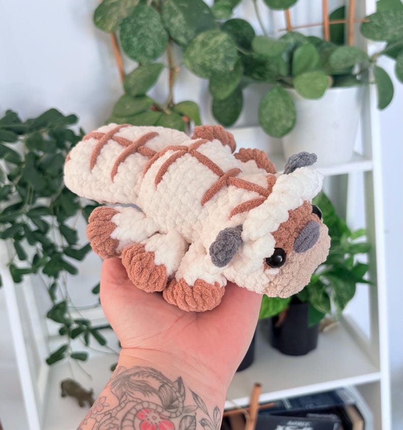 Puede incluir: Un peluche de Appa hecho a mano, de Avatar: La leyenda de Aang. El juguete de ganchillo es blanco con marcas y detalles marrones, incluyendo los pies, las orejas y patrones en forma de cruz en la espalda. El juguete tiene ojos negros y cuernos grises.