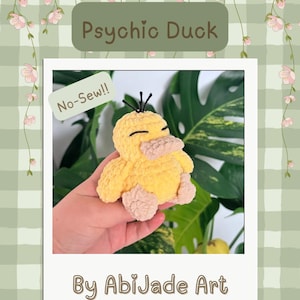 May include: A PDF crochet pattern titled Psychic Duck by AbiJade Art. The image features a yellow plush duck with a light pink beak and feet, three black hair strands, and closed eyes. A green tag on the image reads No-Sew.