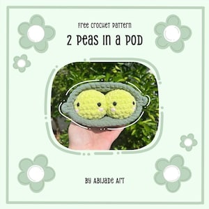 May include: A crocheted pea pod with two yellow peas, each with small black eyes and pink cheeks. The pod is light green, and the background is a soft green with flower accents. Text reads "free crochet pattern" and "2 Peas in a Pod."