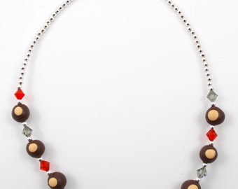 May include: A necklace featuring alternating dark brown beads with tan centers, red diamond-shaped beads, and iridescent crystal beads. The necklace has a silver beaded chain and a silver toggle clasp.