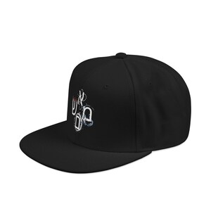 May include: Black flat-brimmed baseball cap with a white, red, and blue abstract design on the front. The cap has a structured fit and a curved brim. The design appears to be hand-drawn.
