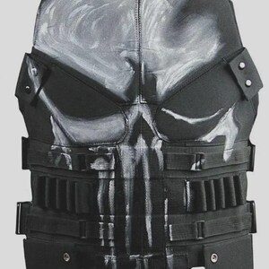 May include: Black tactical vest with a white skull design on the front. The vest has multiple adjustable straps, pouches, and a padded design. The vest is designed for protection and is made of durable materials.