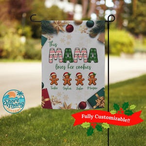 May include: A white garden flag with the text "This MAMA loves her cookies" in green and red. Below are four gingerbread men with names. The flag is decorated with Christmas ornaments and snowflakes. The bottom right corner has a red banner that says "Fully Customizable!!".