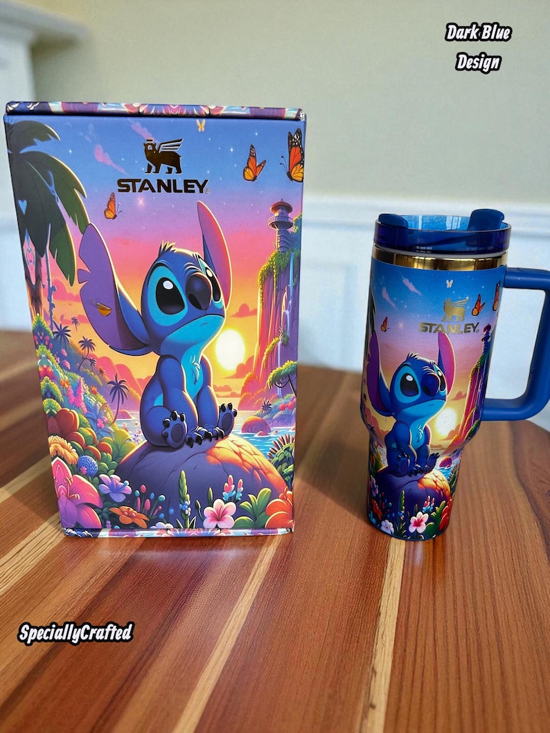 May include: A Stanley travel mug and box set featuring a cartoon character design. The mug and box are decorated with a blue character, butterflies, and a tropical landscape. The box has the text "Stanley" and "Specially Crafted". The mug has a blue handle and lid.