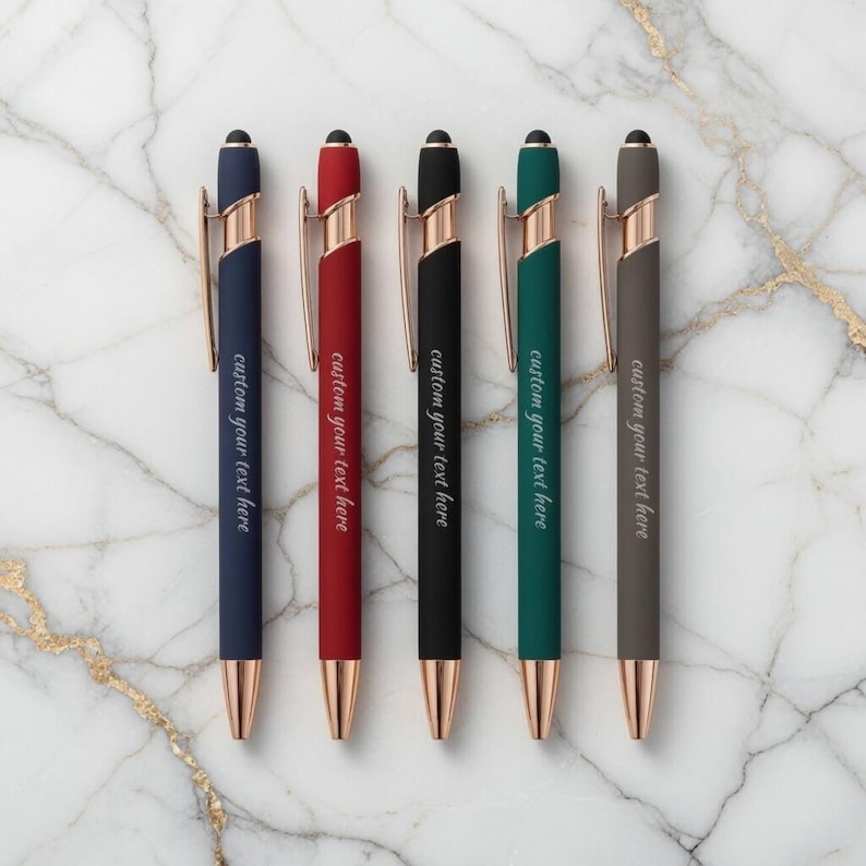 May include: Six pens in navy, red, black, green, and gray, each with a gold-colored clip and tip. The pens have the text "custom your text here" printed on them. The pens are arranged on a marble surface.