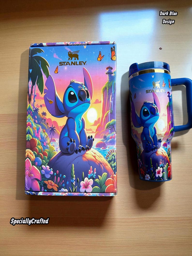 May include: A Stanley brand tumbler and box set featuring a blue cartoon character design. The box and tumbler have a matching design with the character sitting on a rock with a tropical background. The tumbler has a blue handle and lid.