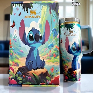 May include: A light blue Stanley mug and box set featuring a cartoon character design. The mug has a handle and a silver rim. The box and mug feature the text "Stanley". The design includes a blue character, butterflies, and a colorful landscape.