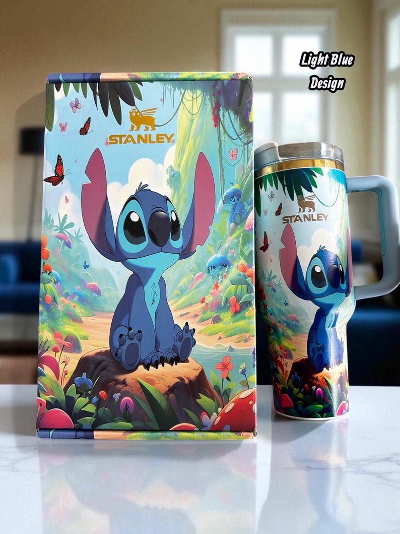 May include: A light blue Stanley mug and box set featuring a cartoon character design. The mug has a handle and a silver rim. The box and mug feature the text "Stanley". The design includes a blue character, butterflies, and a colorful landscape.