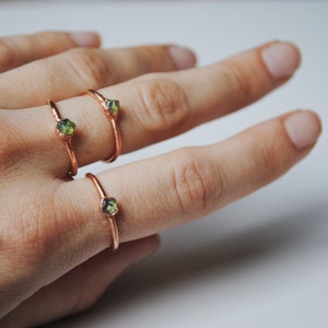May include: Three gold rings with green gemstones. The rings are stacked on a finger.