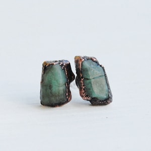 Puede incluir: Un par de pendientes de piedra preciosa verde esmeralda con detalles de alambre de cobre. Los pendientes tienen una forma natural y sin pulir.