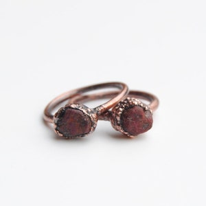 May include: Two copper rings with red gemstone accents. The rings are stacked on top of each other.