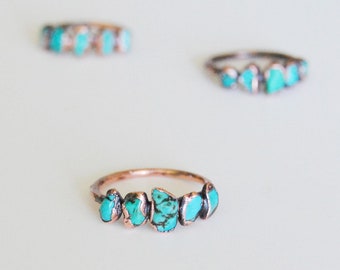 May include: A copper ring with five turquoise stones set in a row. The stones are irregular in shape and have a light blue color.