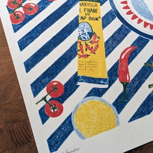 Zoom sur l'illustration. Dessin d'un tube de harissa sur un fond à rayures bleu et blanc. L'illustration est dessinée aux crayons de couleurs. Elle présente également des tomates, piments, ail et coriandre et un plat à motifs, suggérant une ambiance tunisienne. L'illustration est signée de Lucie Leforestier et numérotée, en édition limitée. Le papier est texturé.